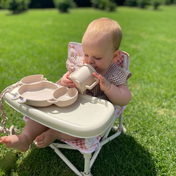 The Coastal patterned Sunkissed Portable Highchair side view with a baby girl eating using Sunkissed Feeding Utensils