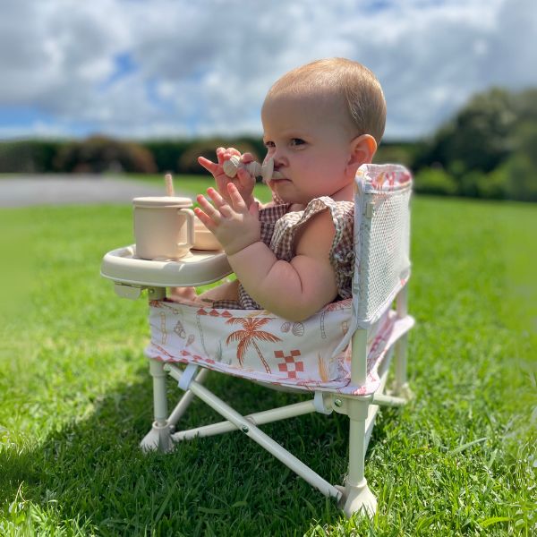 The Coastal patterned Sunkissed Portable Highchair side view with a baby girl eating using Sunkissed Feeding Utensils