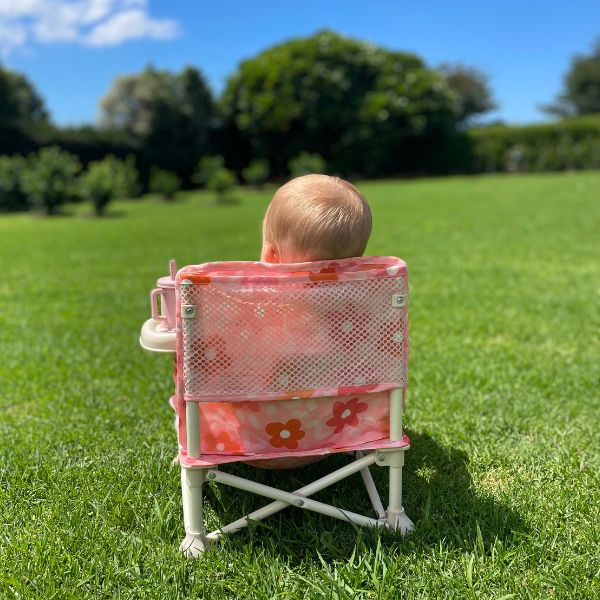 Bloom Portable Baby Highchair with detachable tray. Comes in a carry bag. For kids aged 6M-3Y. Image depicts a happy baby sitting in the chair facing the other way showcasing the mesh pocket on the back.