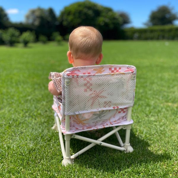 The Coastal patterned Sunkissed Portable Highchair back view with a baby girl sitting in it Showcasing the mesh pocket on the back.